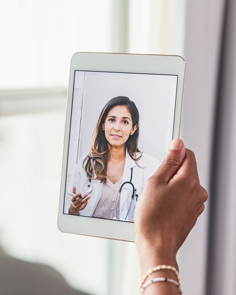 A patient, a Black woman with natural curls, holding a tablet, talking to her physician, a Hispanic women in a white coat.