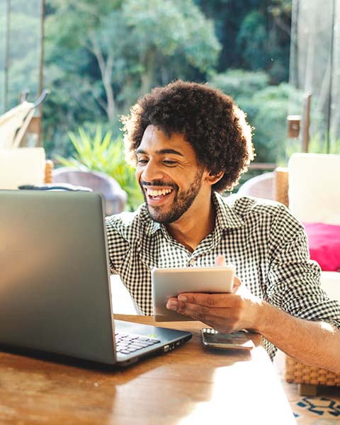 Physician, a Black man, at his home office with his notepad, cell phone and laptop, smiling and typing his cover letter.