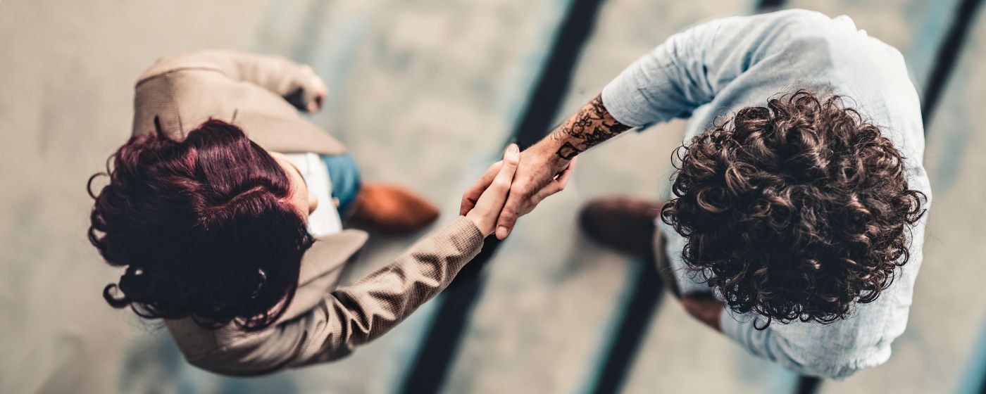 Birds eye view of two physicians shaking hands, one is an Asian woman, the other an Indian man, both professionally dressed.