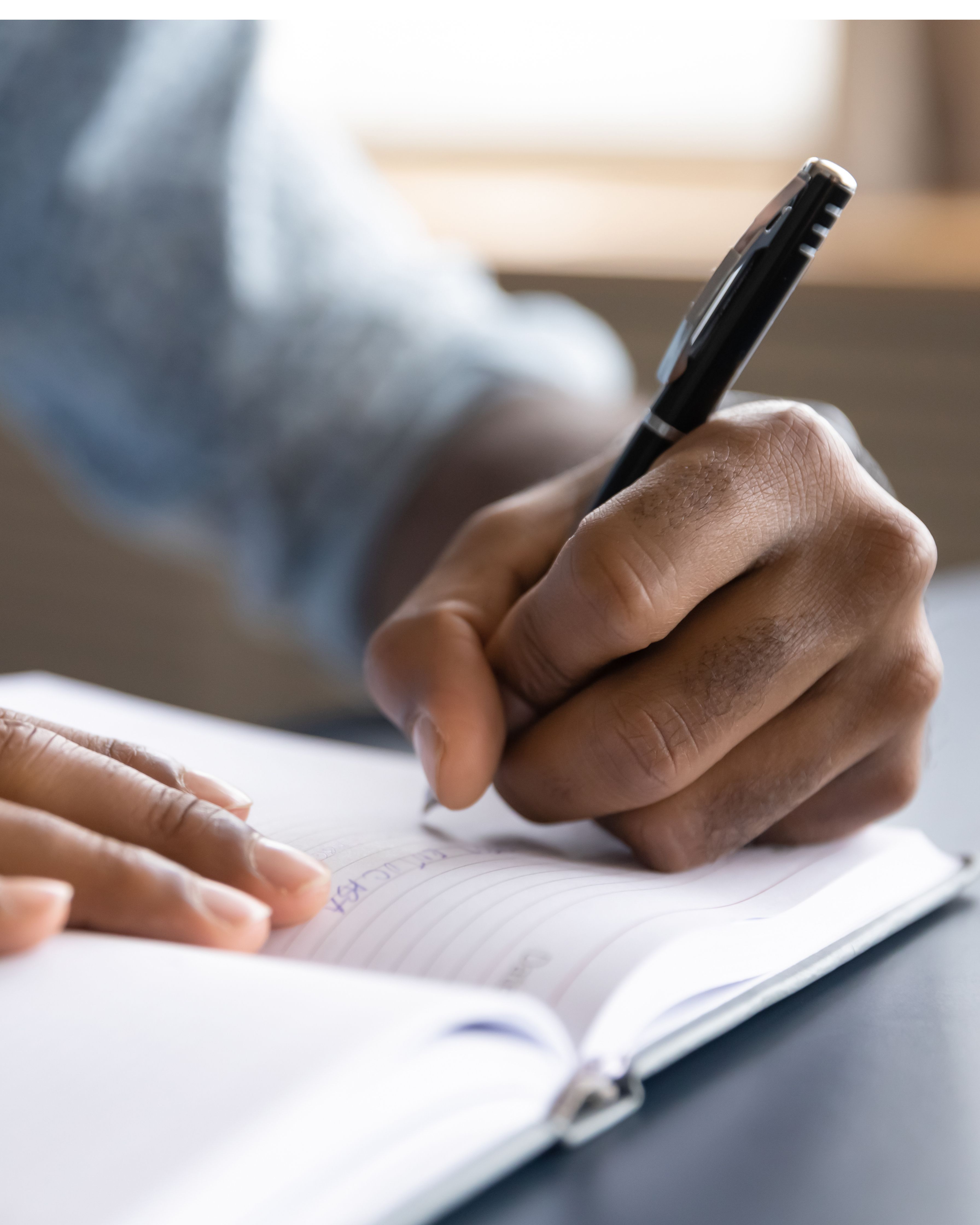 Close up of physician's left hand writing interview questions in a notebook.