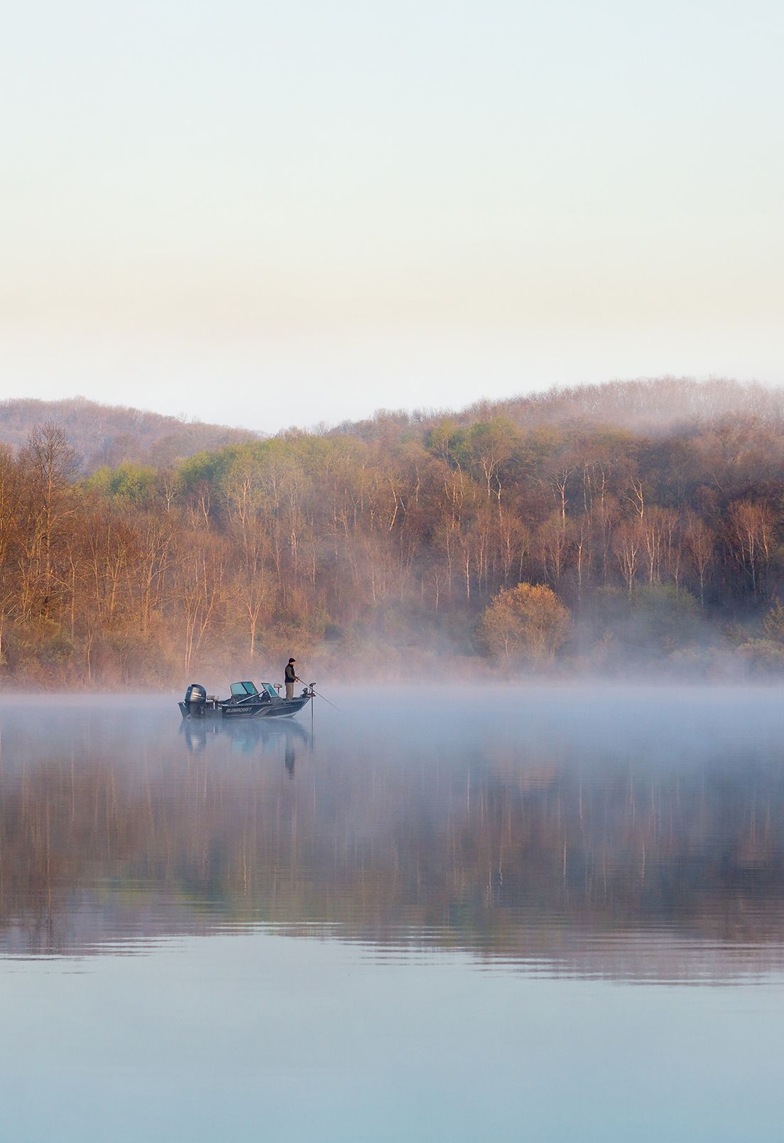 Representing Wisconsin is a view of a foggy river at dusk with a fisherman on a boat in the distance.