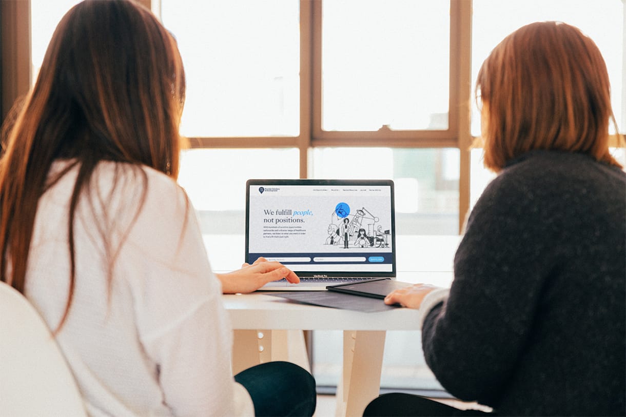 Looking over the shoulder of two senior medical residents, white women, together looking at jobs on PS&D’s website.