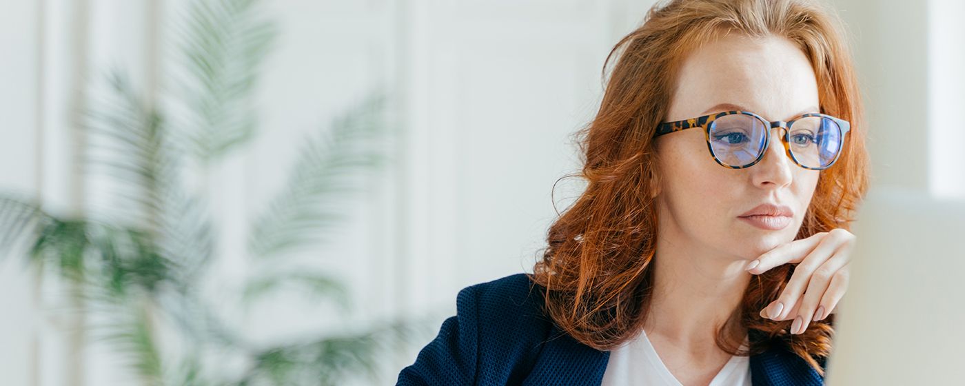 An Family Medicine physician, a white woman with red hair and glasses, at her computer, researching jobs on PS&D's website.